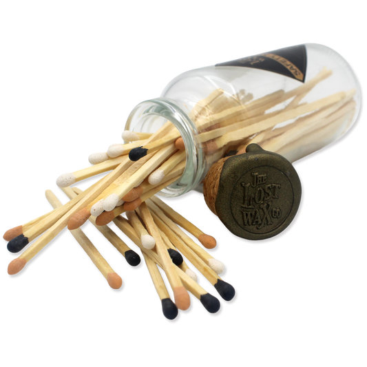 A clear glass bottle filled with safety matches from The Lost Wax Co., sealed with a cork stopper.
