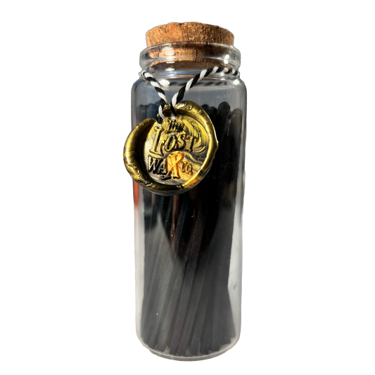 Glass jar with cork lid containing black safety matches and a gold seal labeled 'The Lost Weft Co.' on a white background.