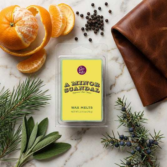 Wax melt package labeled 'A Minor Scandal' surrounded by decorative elements on a marble surface.