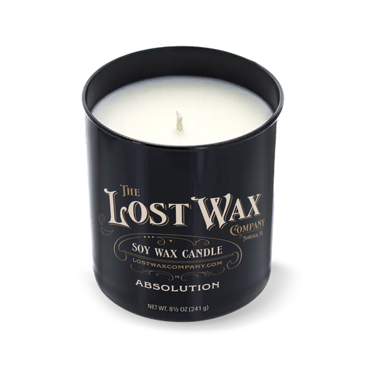 A black cylindrical scented candle jar with a matching lid leaning against it on a white background. The label reads 'The Lost Wax Company' and 'Absolution'.