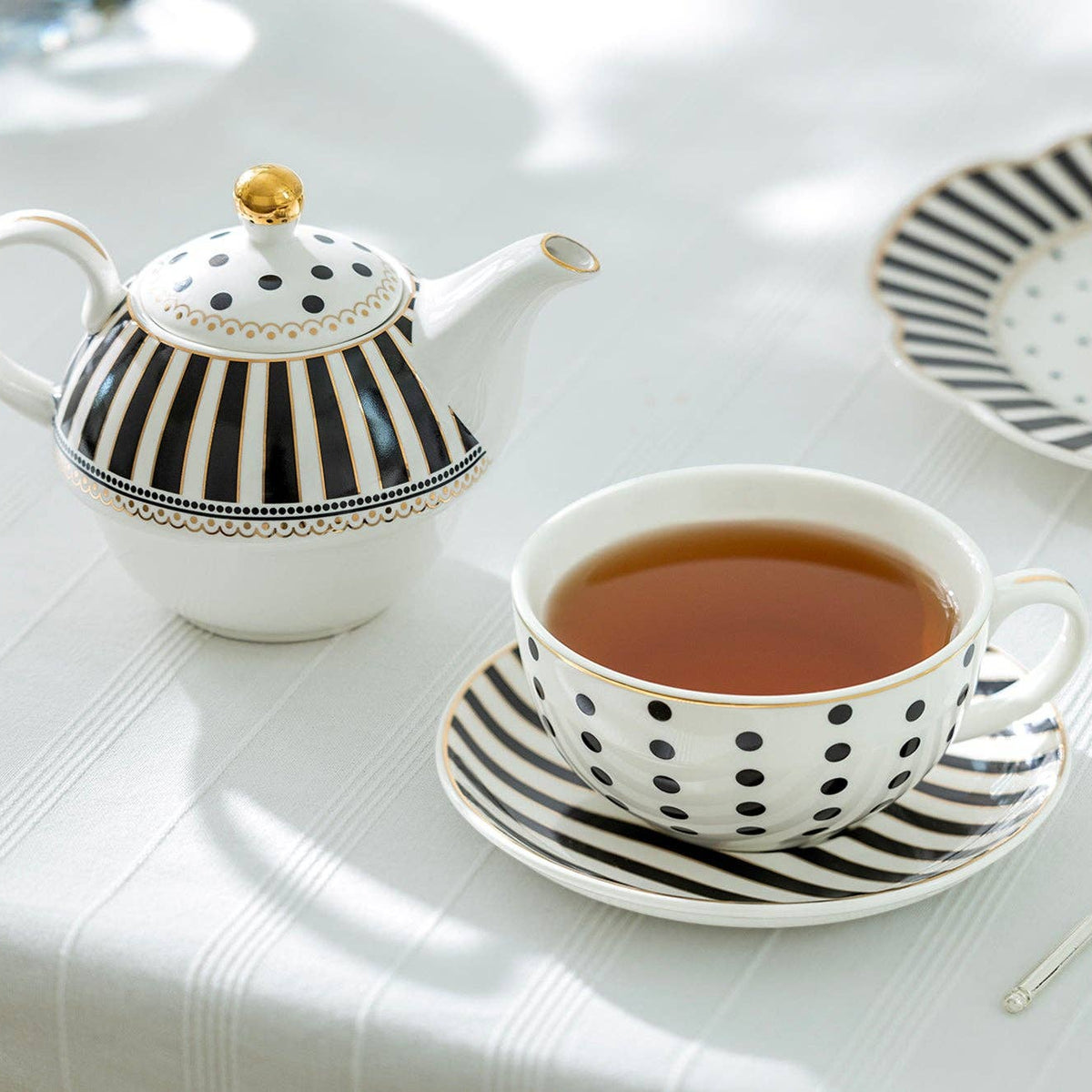 Tea set with a teapot, cup, and saucer on a white tablecloth.