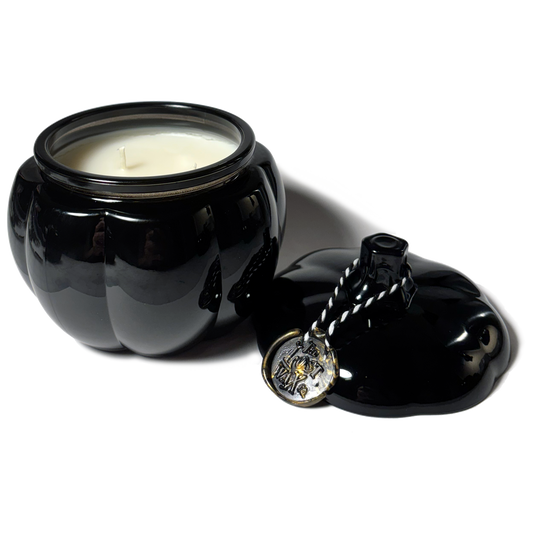 Black glasspumkin-shaped jar with a candle inside and a decorative lid on a white background