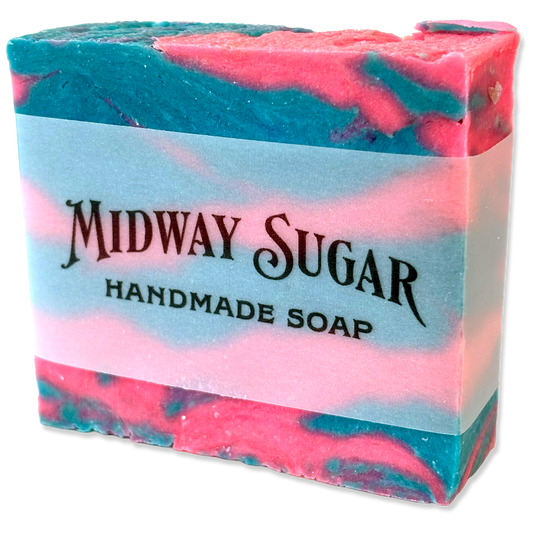 A rectangular bar of handmade soap with a pink and teal marbled pattern, wrapped in a white paper band that reads 'MIDWAY SUGAR HANDMADE SOAP'.