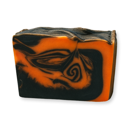 A rectangular bar of handmade soap with a marbled swirl pattern of vibrant orange and black, photographed on a clean white background.
