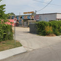 Building with 'Perro Blanco' sign and colorful mural, surrounded by greenery and a no parking sign.