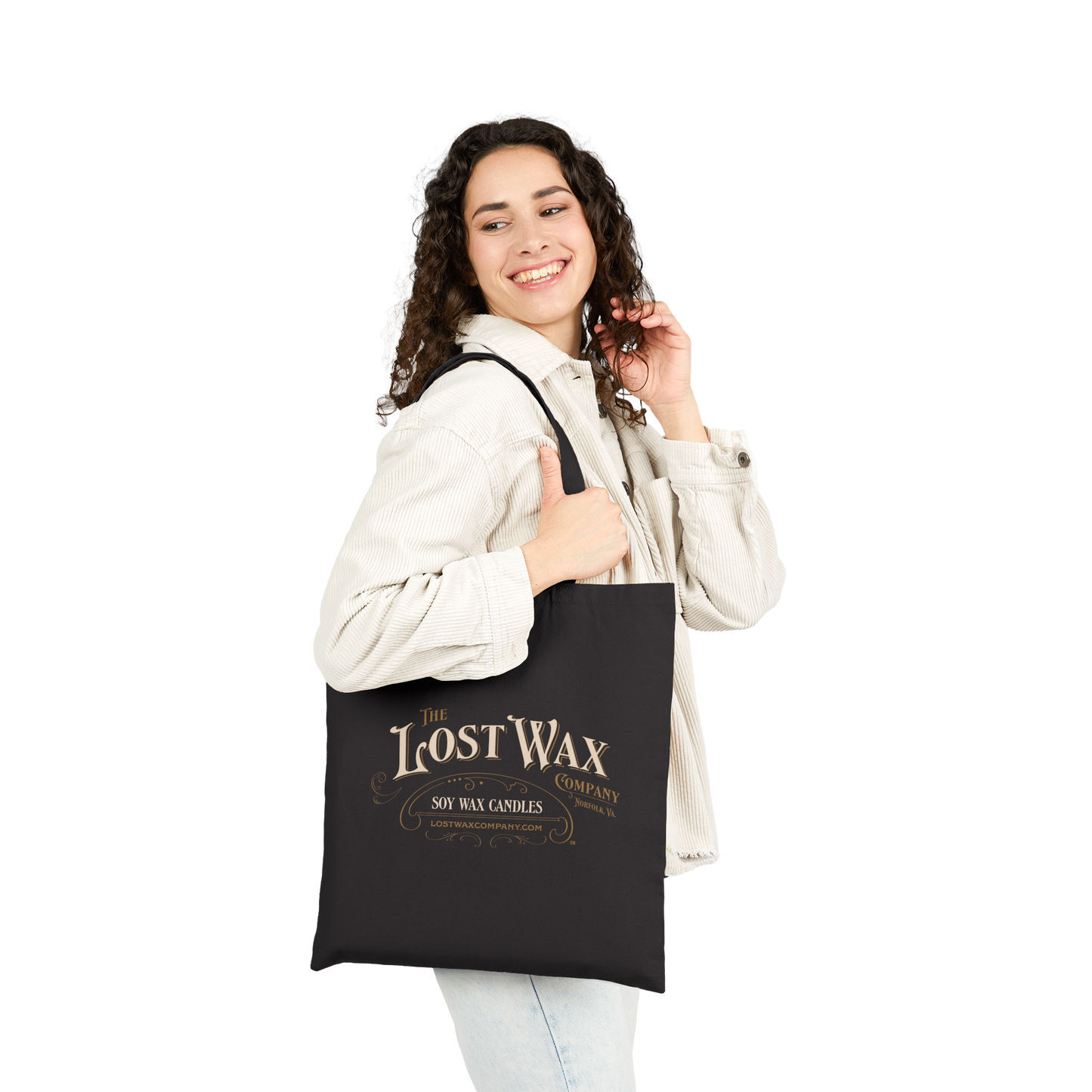Woman holding a black tote bag with 'The Lost Wax Candle Company' branding on a white background