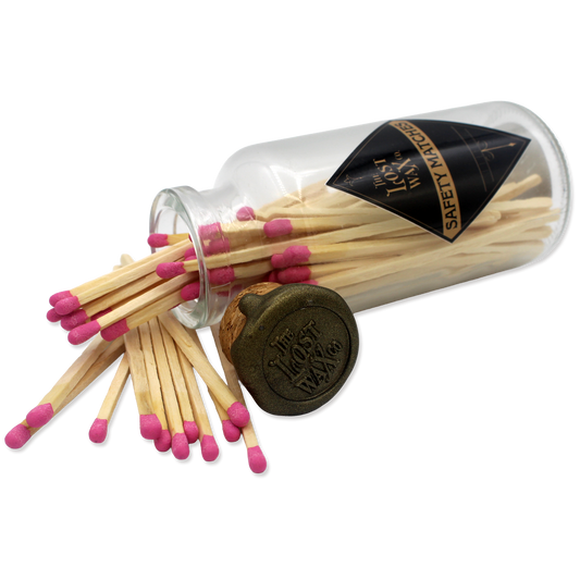 Glass jar with cork lid containing pink-tipped safety matches branded 'The Lost Wax Co'.
