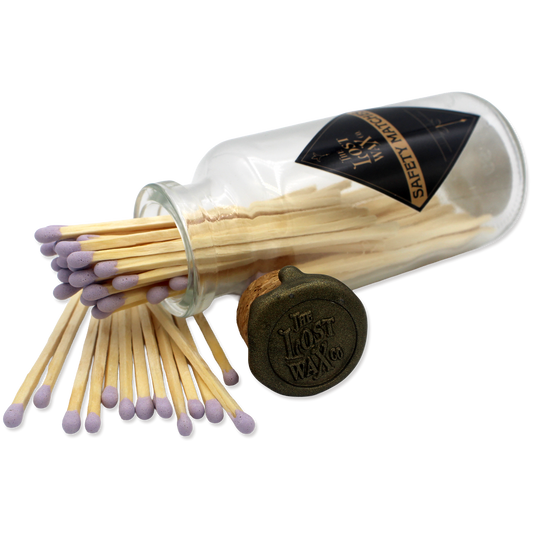 Glass jar with cork lid containing lavender-tipped safety matches branded 'The Lost Wax Co'.