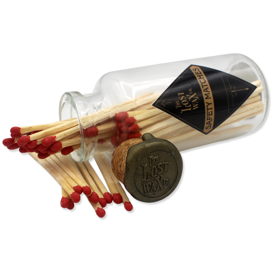 Glass jar with cork lid containing red safety matches branded 'The Lost Wax Co'.