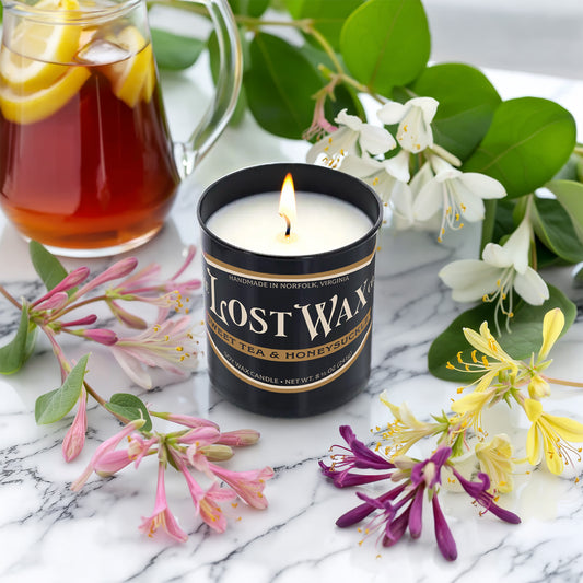 Lost Wax candle with a pitcher of iced tea and honeysuckle flowers on a marble surface