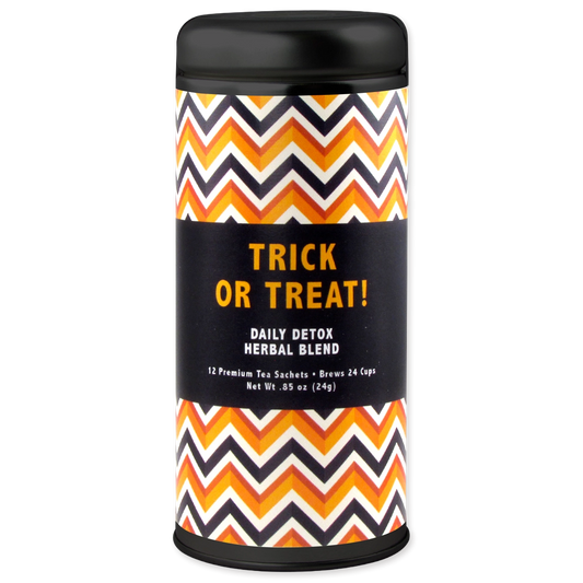 A cylindrical tea sachet canister with a black lid and base, featuring a black central label with orange text reading 'TRICK OR TREAT! DAILY DETOX HERBAL BLEND' and a black, orange, white, and gray chevron pattern on the sides. The canister is centered on a plain white background.