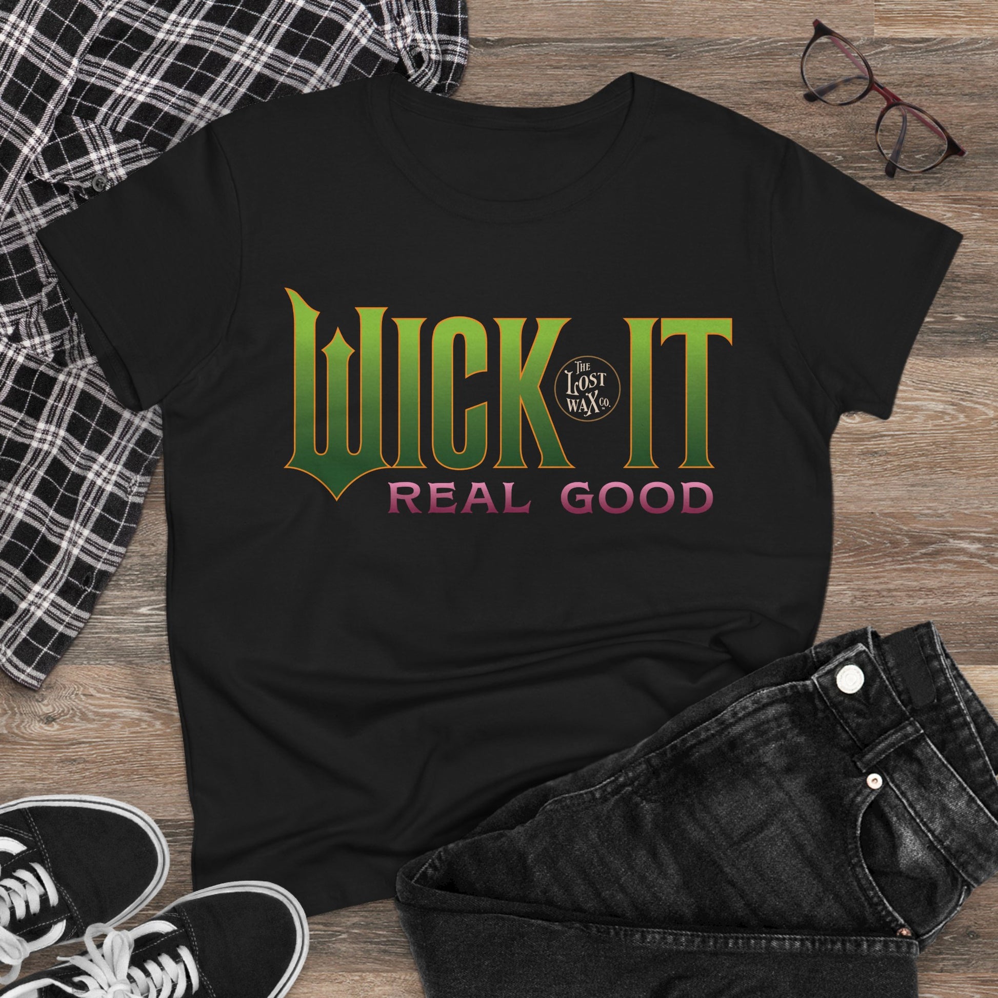 Black t-shirt with 'Wick It Real Good' text on a wooden surface with casual items.