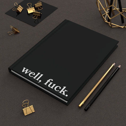 Black notebook with 'well, fuck.' text on a dark surface with office supplies.