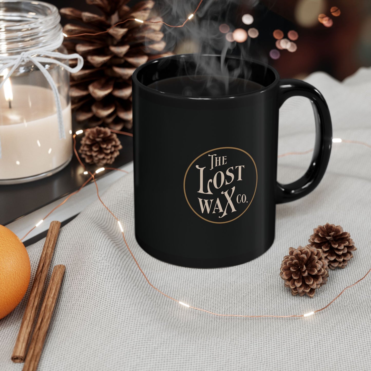 Black mug with 'The Lost Wax Co.' logo on a table with decorative items