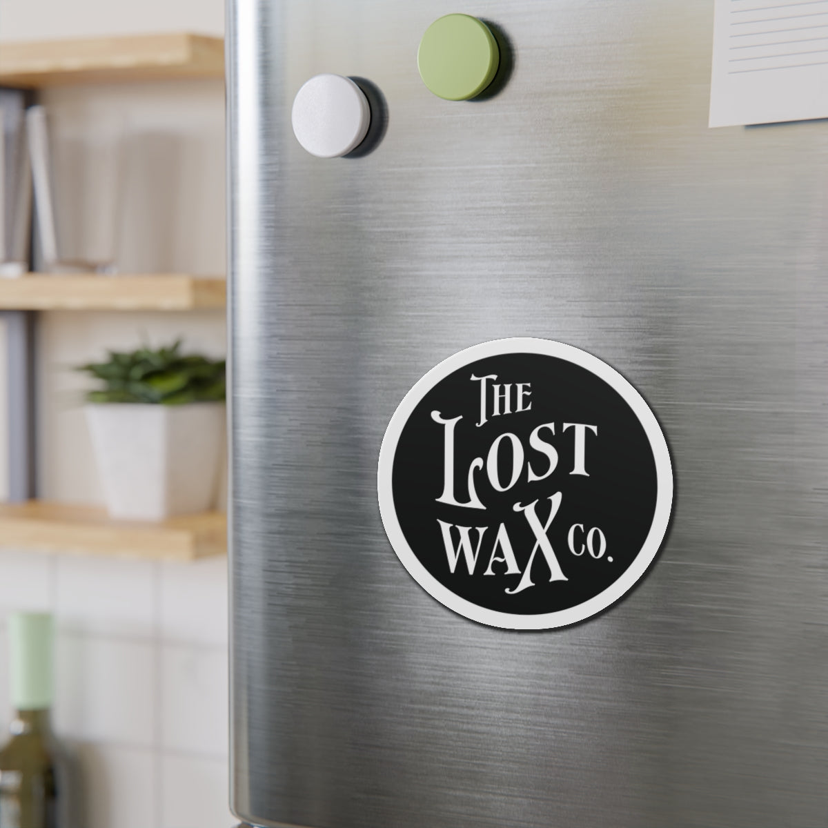 Round magnet with 'The Lost Wax Co.' on a metallic surface