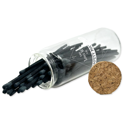 Clear glass tube with black safety matches and cork lid on a white background
