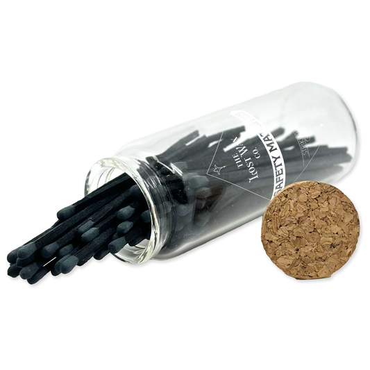 Clear glass tube with black safety matches and cork lid on a white background