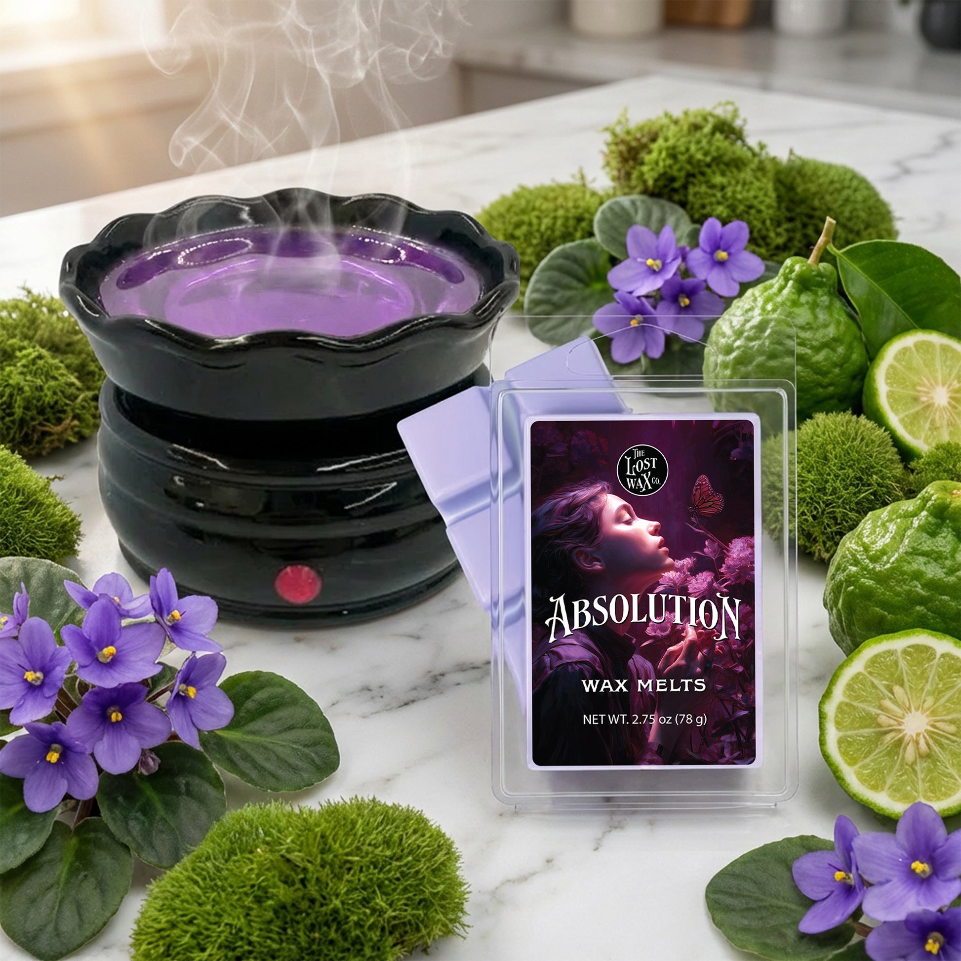 Wax melter with purple wax and 'Absolution' packaging surrounded by greenery and flowers on a marble surface.