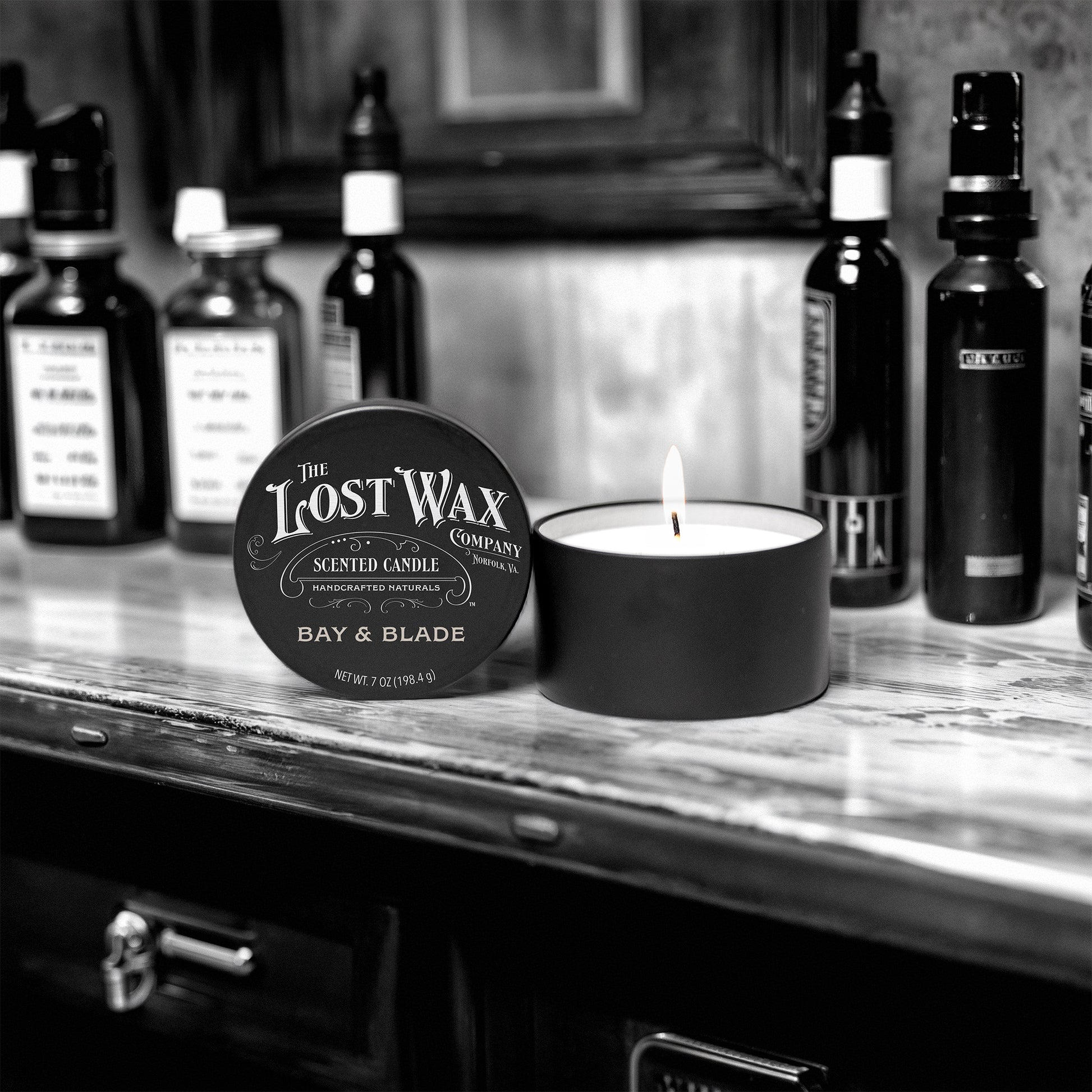 Candle and container labeled 'The Lost Wax Company' on a shelf with bottles in the background