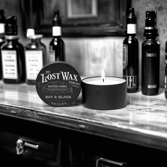 Candle and container labeled 'The Lost Wax Company' on a shelf with bottles in the background