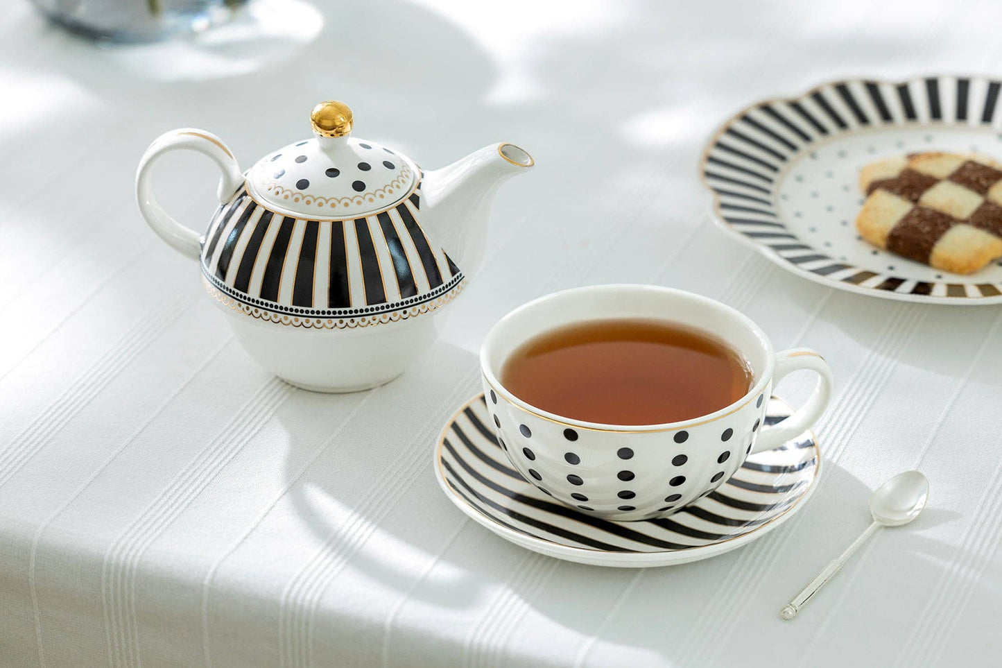 Tea set with a teapot, cup, and saucer on a white tablecloth.