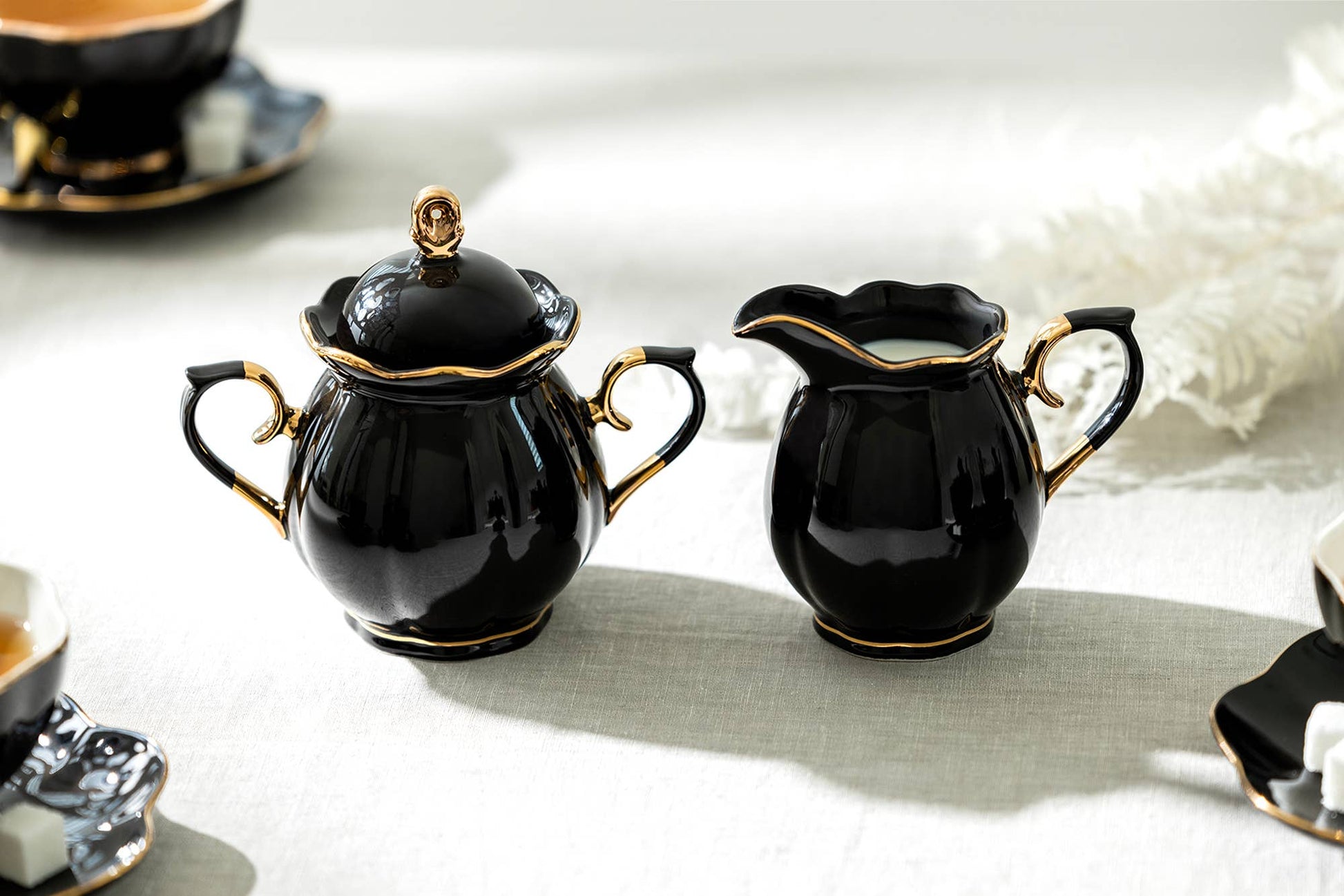 Black ceramic teapot and creamer set with gold accents on a light surface.