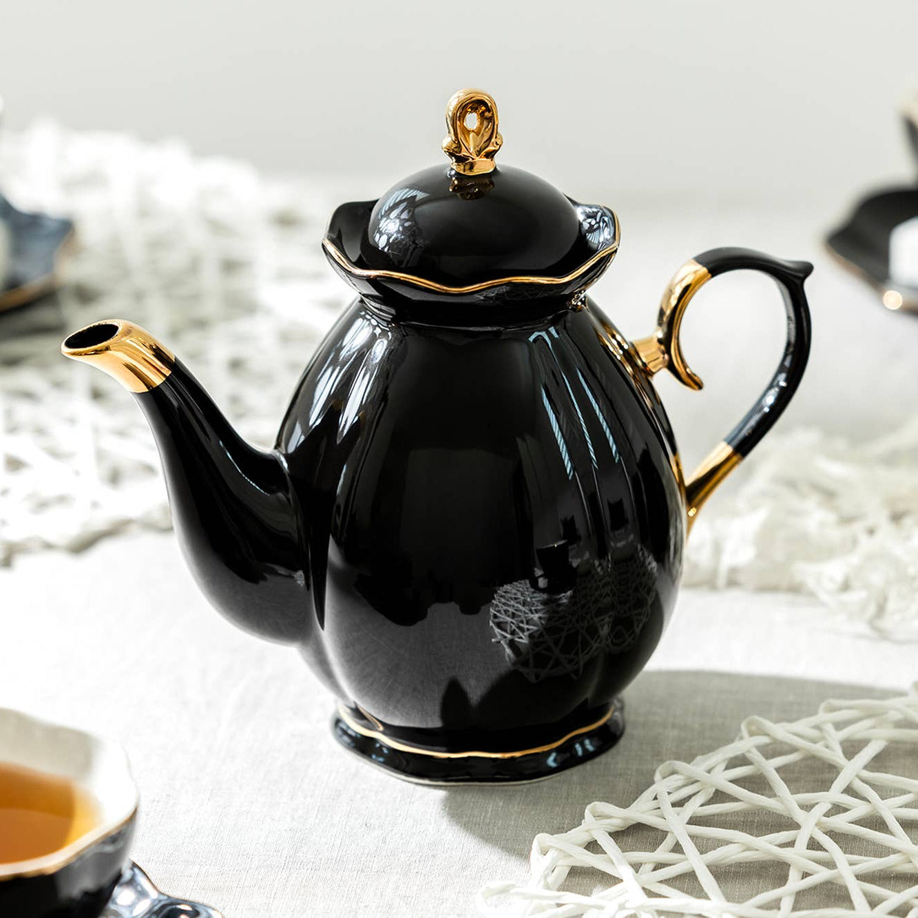 Black teapot with gold accents on a white surface with tea cups and saucers.