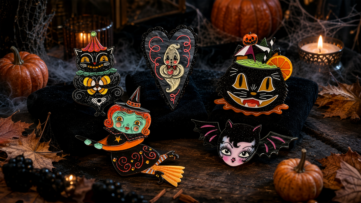 A set of Halloween-themed acrylic pins displayed on a black velvet cloth, surrounded by autumn props like small pumpkins, spiderwebs, and lit candles.