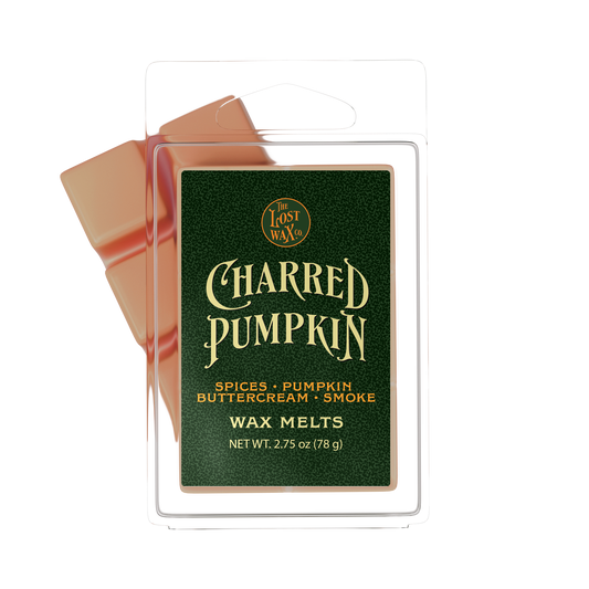 Lost Wax Co. Charred Pumpkin scent wax melts in a clear plastic clamshell package with a dark green label and orange-colored wax visible behind it on a white background.