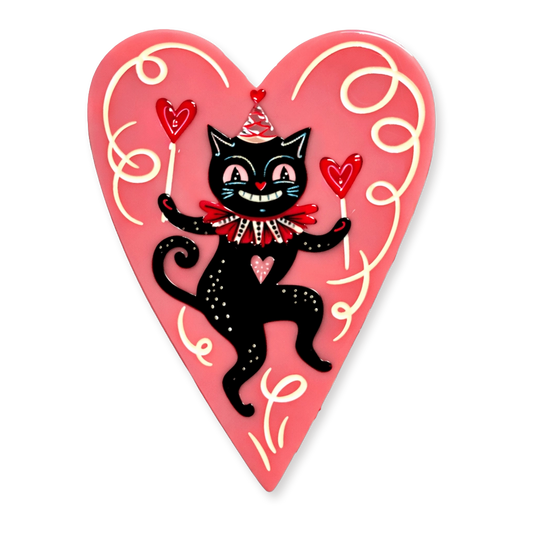 A heart-shaped decorative brooch featuring a black cartoon cat wearing a red bow tie and party hat, holding red hearts, on a pink background with cream swirl details.
