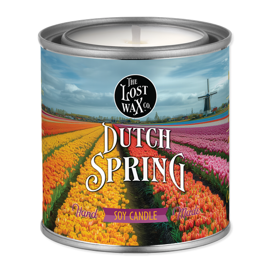 Candle in a can labeled 'Dutch Spring' with a scenic design on the label.