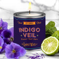 Candle in a can labeled 'Indigo Veil' by The Lost Wax Co., surrounded by purple flowers and a lime.