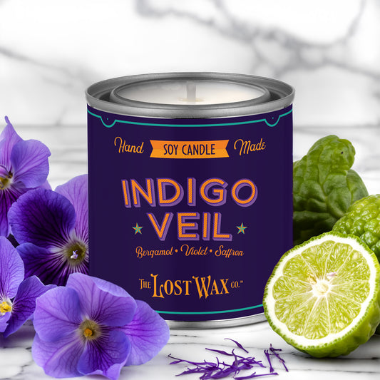 Candle labeled 'Indigo Veil' by The Lost Wax Co. with purple flowers and a lime on a white background