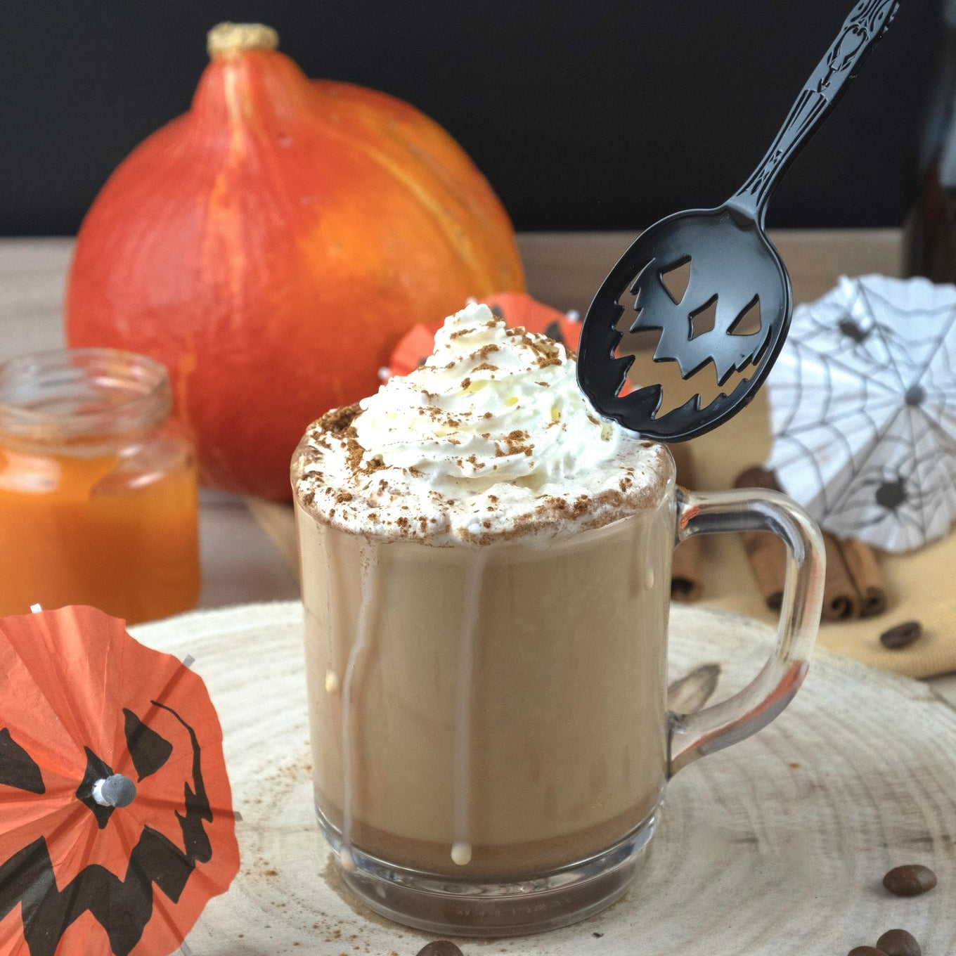 Halloween-themed coffee drink with whipped cream and a black spoon on a wooden surface.