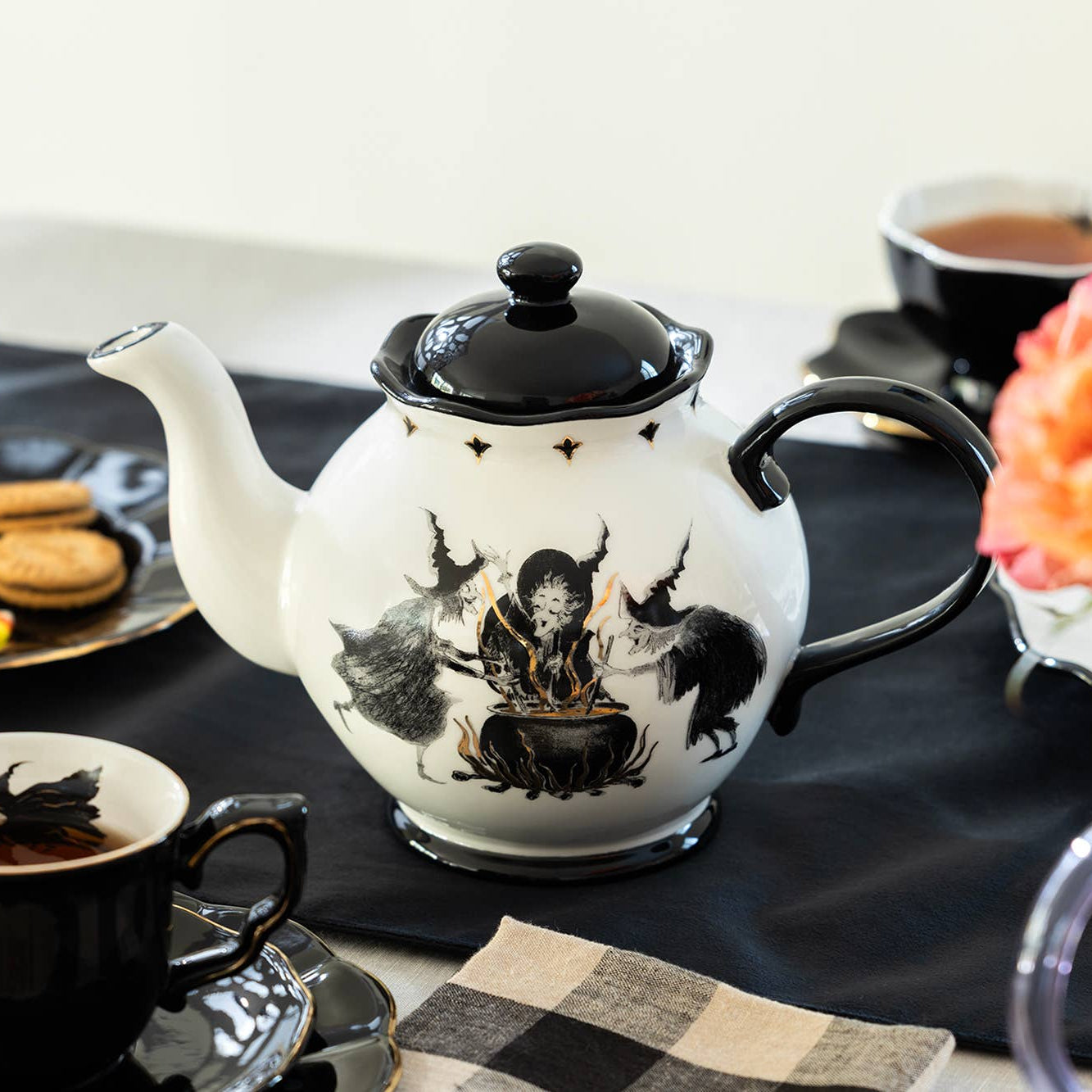 Teapot with witch design on a table with coffee cups and flowers