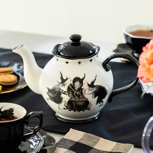 Teapot with witch design on a table with coffee cups and flowers