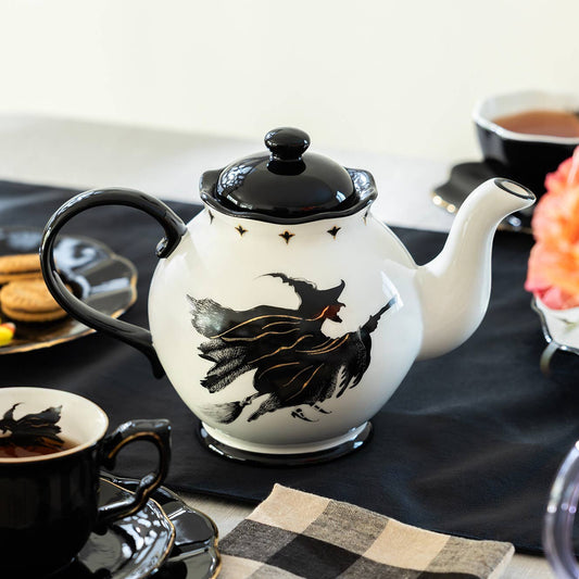 Teapot with witch design on a table with coffee and flowers
