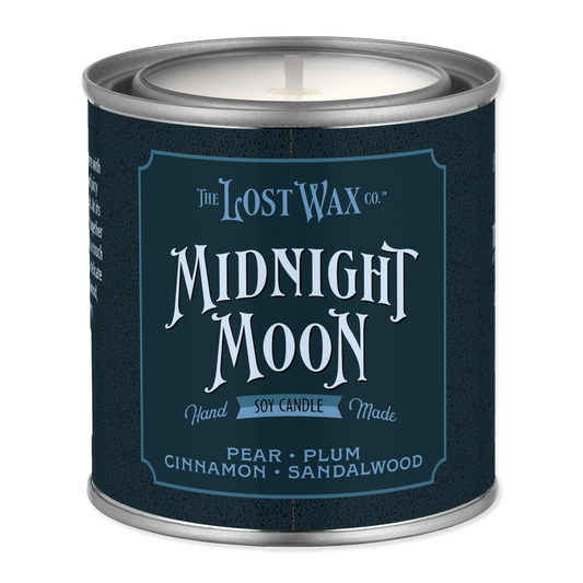 A metal tin candle from The Lost Wax Co. named 'Midnight Moon' in pear, plum, cinnamon, and sandalwood scents, featuring a dark navy blue label with white text.