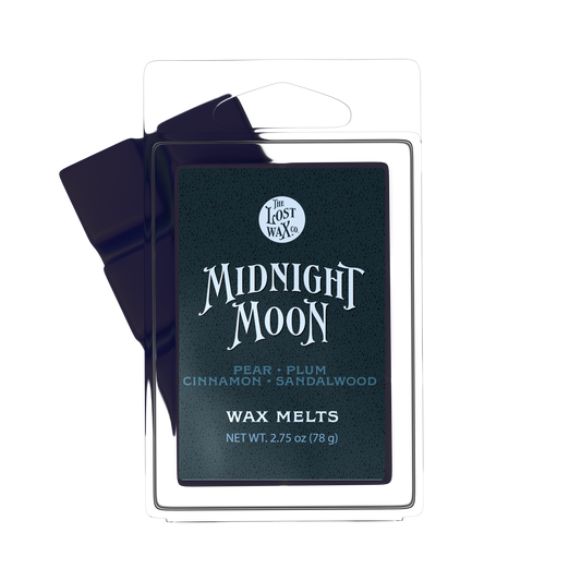 A package of Lost Wax Co. Midnight Moon wax melts, featuring a dark green label with white text inside a clear plastic clamshell container, with a dark purple wax melt bar partially visible behind it on a white background.