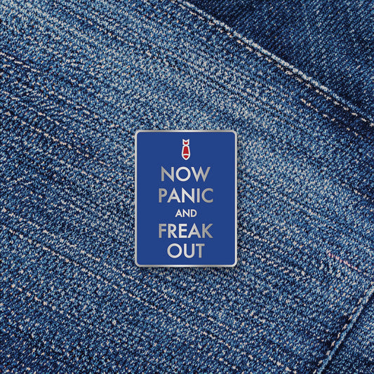 Blue enamel pin "Now Panic and Freak Out" by Studio Ten Design. Shown on a denim background.