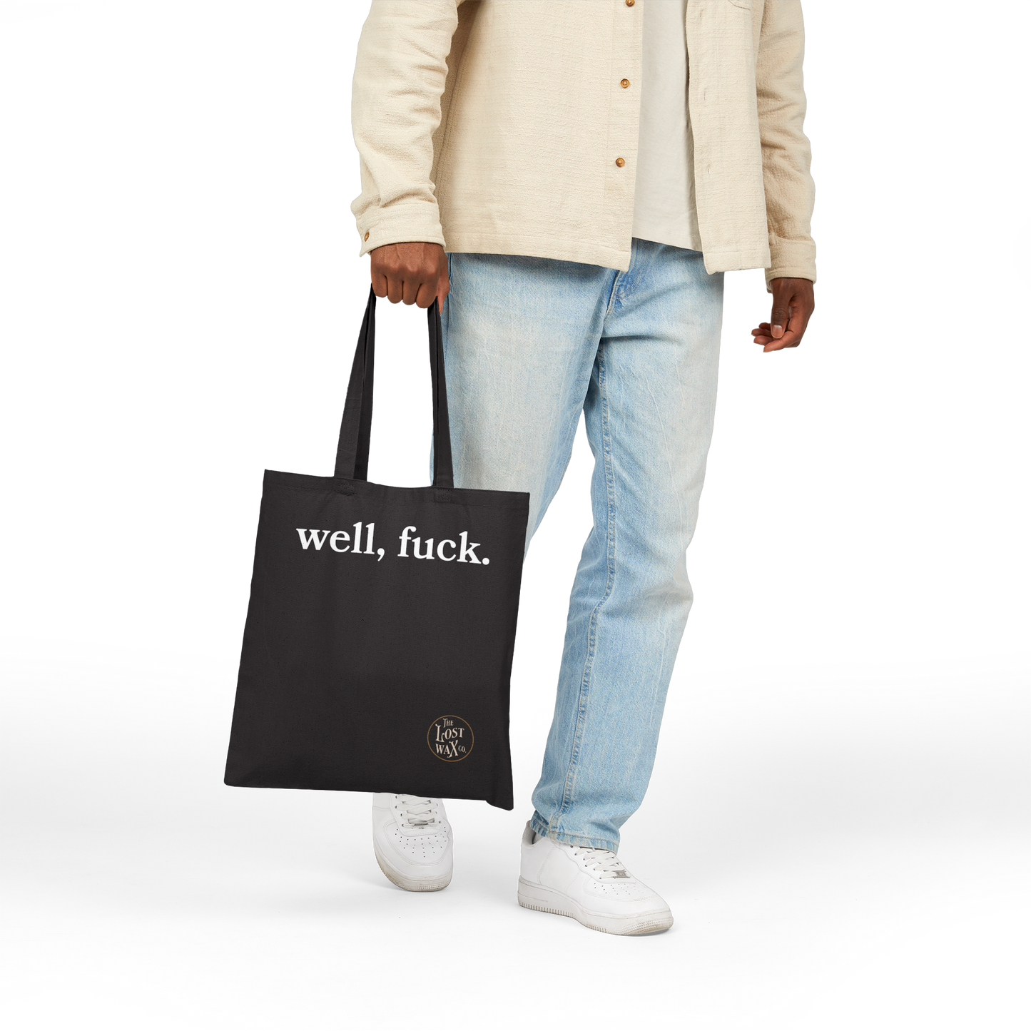 Person holding a black tote bag with 'well, fuck.' text on a white background
