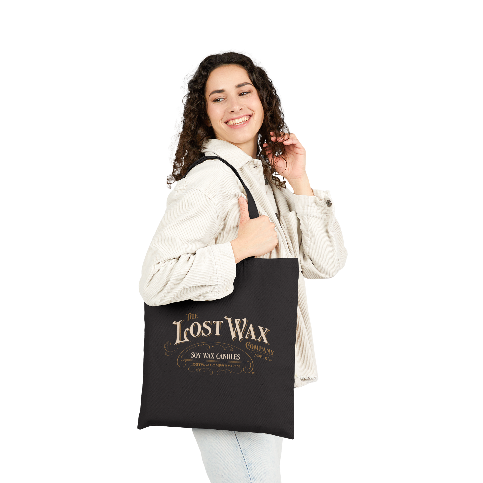 Woman holding a black tote bag with 'The Lost Wax Candle Company' branding on a white background