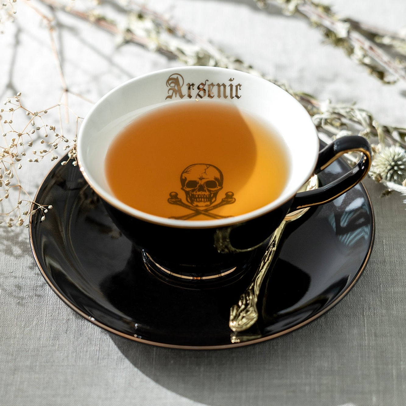 Teacup with 'Arsenic' and skull & crossbones decorations on a saucer with decorative elements