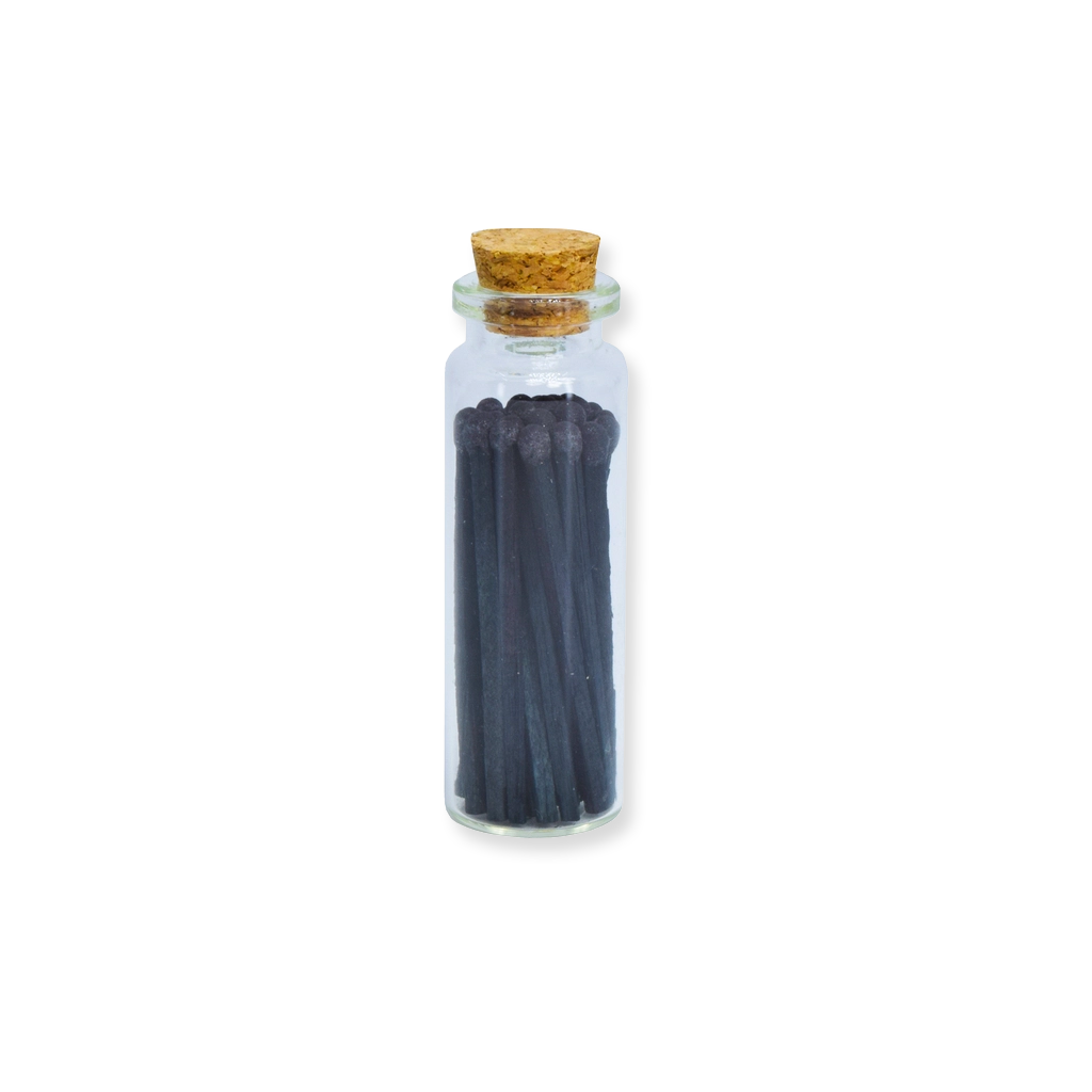 Small glass bottle with cork lid containing dark sticks on a white background