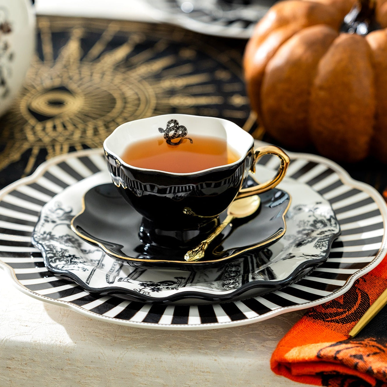 Teacup with saucer and spoon on a Halloween-themed table setting with pumpkins and skull decorations.