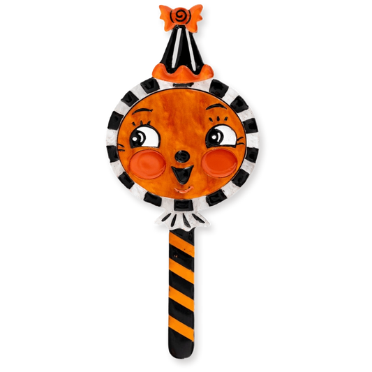 A Halloween-themed decorative candy-shaped brooch with a round orange face, black-and-white striped border, black-and-orange striped handle, and an orange-and-black pointed hat with a small black spider on top, shown on a plain white background.