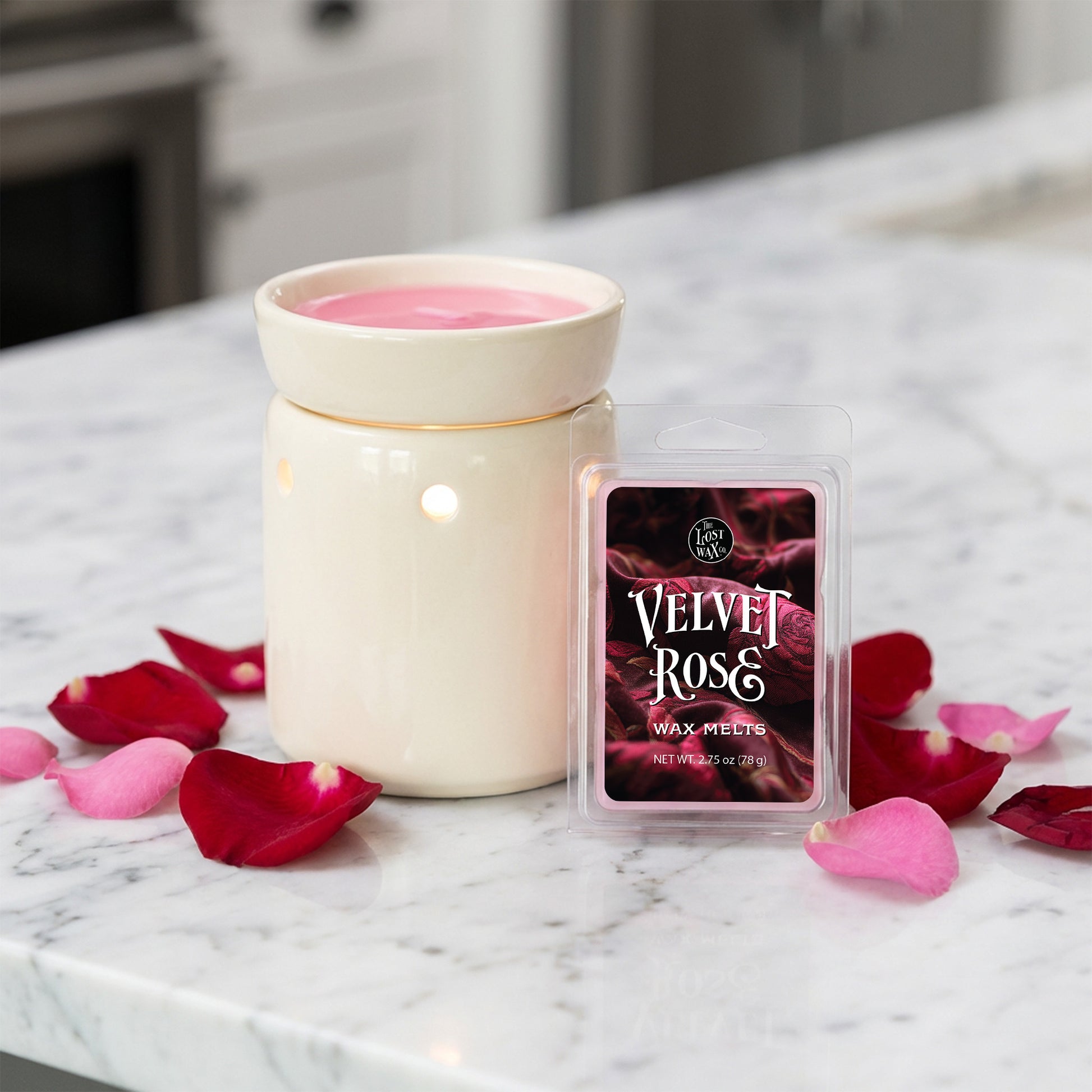 White wax warmer with pink wax and a 'Velvet Rose' wax melt package on a marble surface with rose petals.